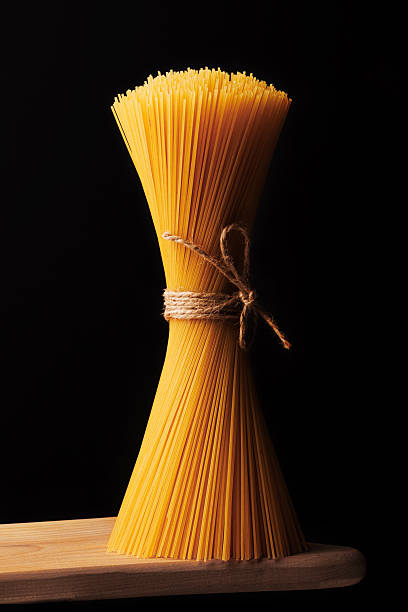 istock Spaghettini tied with thread stand on a wooden board on a black background close-up 2246854228