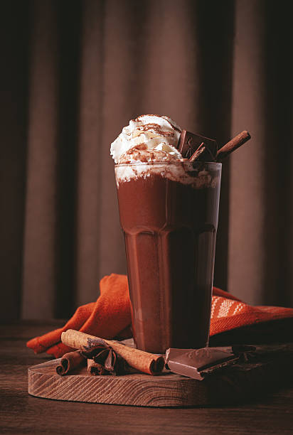 hot chocolate drink, topped with whipped cream, chocolate shavings, and a cinnamon stick