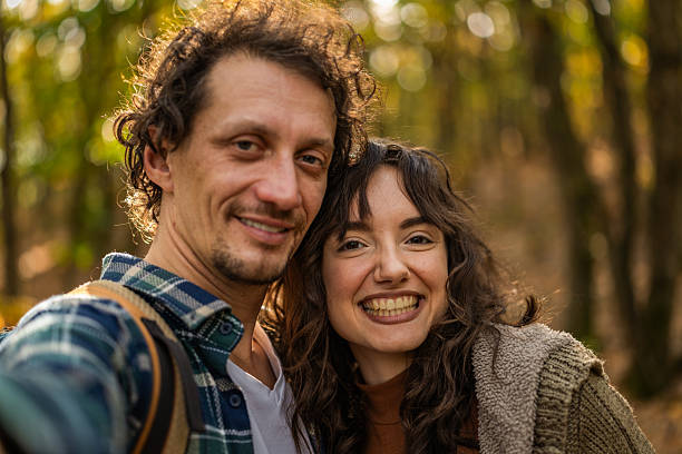 istock Happy couple of backpackers having fun while taking a selfie with mobile phone during autumn day in forest. 2246859196