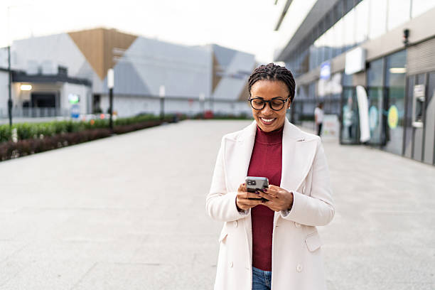 istock Professional black woman smiling, using smartphone outdoors 2246866557