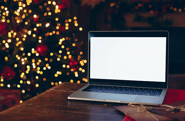 istock Laptop with a white screen mockup placed on a dark wooden table indoors against a background of a brightly lit, blurred Christmas tree. 2246867896
