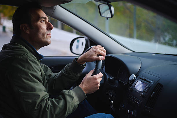 A man concentrates while driving, gripping the steering wheel with the dashboard and side mirror visible, conveying focus, safety, and everyday travel.