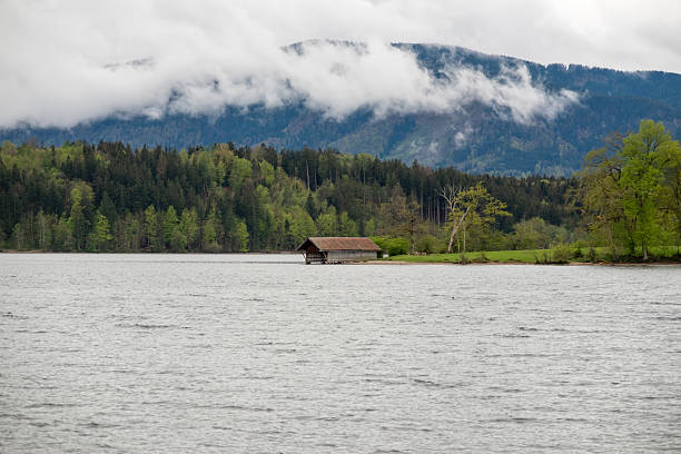 A cozy house sits by a tranquil lake, with mountains and lush greenery in the background. Peaceful natural scenery perfect for travel, architecture, and outdoor photography.