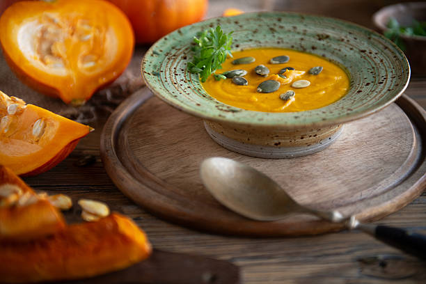 Overhead shot of pumpkin soup served in a rustic ceramic bowl next to a wooden plate filled with fresh squash pieces. Natural light autumn food scene with warm tones and organic ingredients.