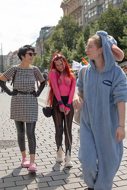 three people walking prague pride march wearing colorful outfits and playful costume, laughing and interacting on sunlit cobblestone street CZ, Prague, Na prikope, 2.8.25