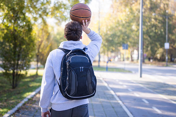 istock Student With Backpack Throwing Basketball On Park Path In Sunny Fall Day 2246880626
