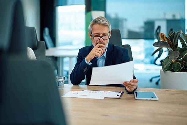 istock Mature businessman reading report, analyzing business documents in office 2246882571