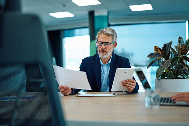 istock Mature adult businessman comparing documents using digital tablet in office 2246882586