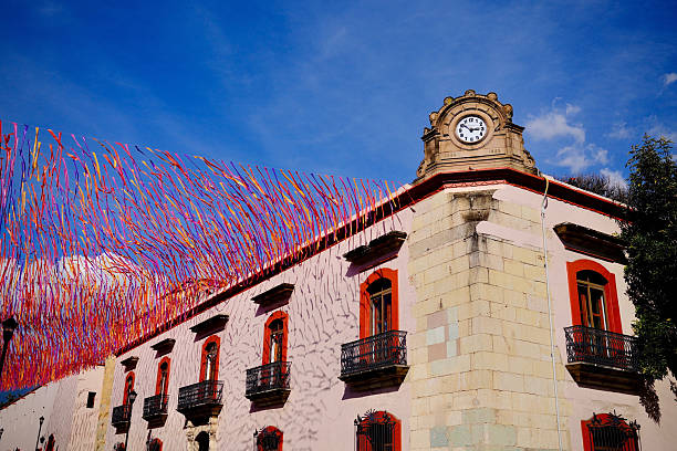 A historic clock tower rises above a building draped in colorful festival ribbons.