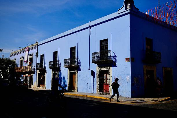 Oaxaca de Juarez, Oaxaca, Mexico – November 6, 2025: A vivid blue building sits half in shadow with silhouetted pedestrians passing by.