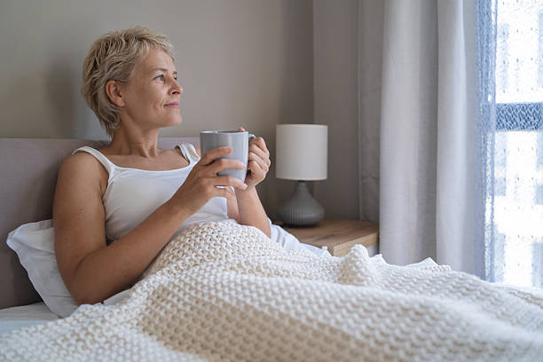 istock Contemplative woman looking outside with cup in bed 2246884475