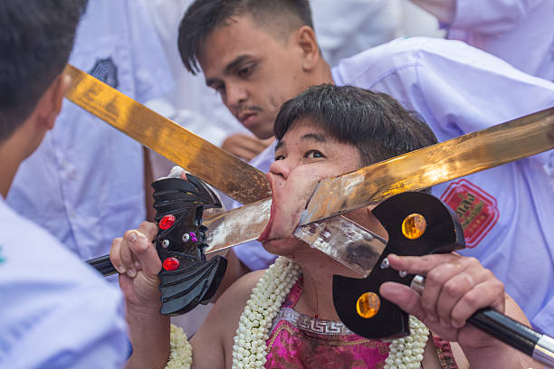 Phuket, Thailand - November 06 2025: Devotee with large metal swords piercing his cheeks during the annual Vegetarian Festival in Phuket. This ritual highlights spiritual devotion and pain endurance.