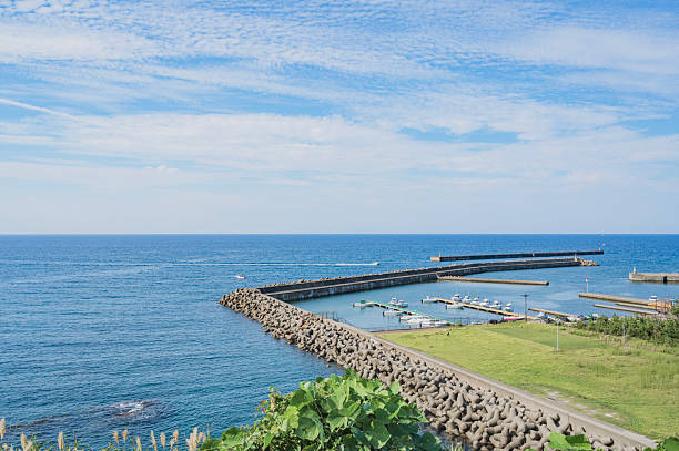 Shari District, Japan - June 2, 2023: The waterfront of Utoro Fishing Port includes commercial fisheries and tourist resorts. Background shows the green hills of Utorokagawa. Spring afternoon with overcast skies.