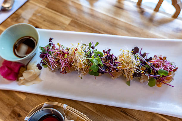 Fresh sushi roll topped with vibrant microgreens and sprouts served with soy sauce and pickled ginger. Gourmet Japanese cuisine on a white rectangular plate. Asian food presentation.