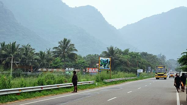 Kumily, Kerala, India - November 15, 2025: Ayyappa devotees walk along the Theni–Kumily Highway, beginning their early Sabarimala padayatra through misty hills and lush rural landscapes