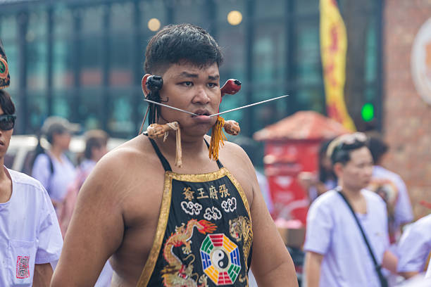Phuket, Thailand - November 06 2025: A devotee exhibits spiritual devotion during the vibrant Phuket Vegetarian Festival, featuring elaborate cheek piercings with skewers and traditional ceremonial