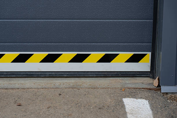 istock Industrial garage door bottom section with yellow black hazard strip and textured panel surface above concrete apron, showing safety marking placement for controlled facility access 2246916389