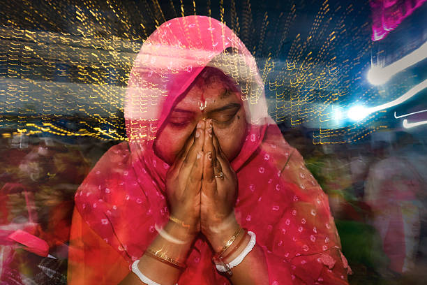 A young and attractive Indian woman prays in her home during Diwali. She is traditionally dressed as she sits in her home with her hands together at chest level. She is happy and full of joy.