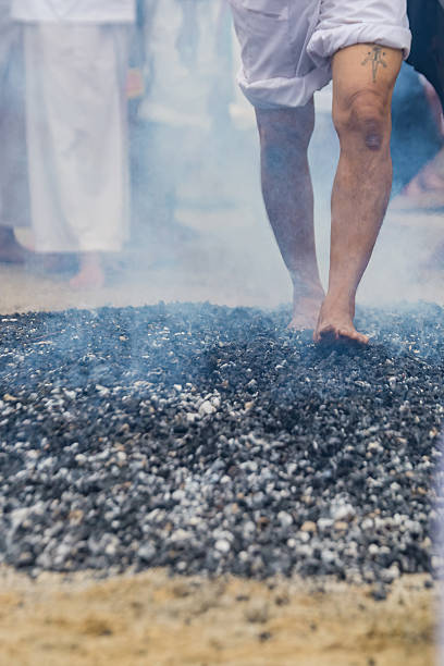 Phuket, Thailand - November 06 2025: Devotees bravely navigate smoldering coals barefoot amidst smoke during a vibrant spiritual firewalking ritual, showcasing profound faith and cultural tradition.