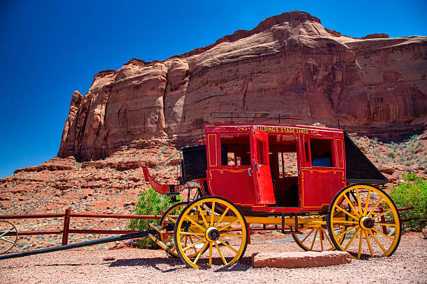 Red carriage standing on desert ground with iconic rock formations in Monument Valley.