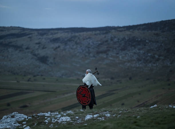 Viking warrior with axe standing on mountain cliff, wearing fur cloak and leather armor, overlooking dramatic landscape. Historical Nordic fighter, strength and adventure concept.