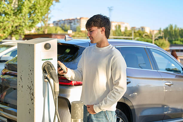 istock Young man charging electric vehicle using smartphone app 2246929496