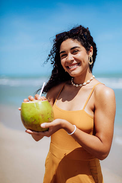 istock Smiling Woman Holding a Coconut by the Beach 2246929868
