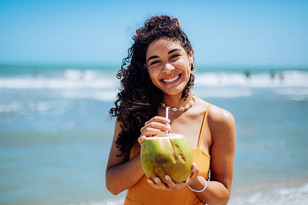 istock Smiling Woman Holding a Coconut by the Beach 2246929890