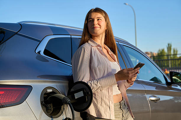istock Young woman charging electric car and using phone 2246930096