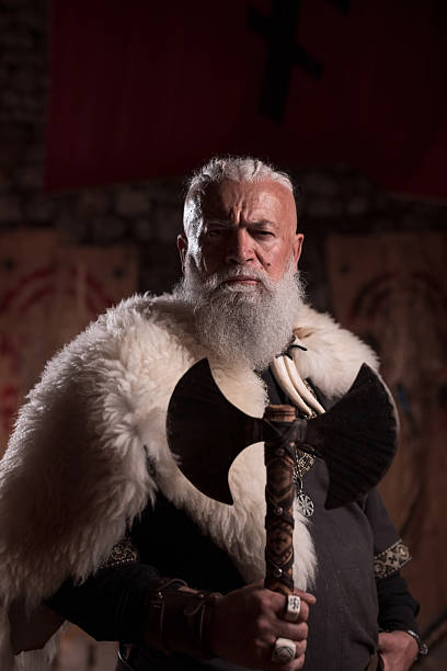 istock Rugged Viking warrior as a king or hero with a white beard, dressed in traditional armor, holding a battle axe, inside a medieval hall, intense and fierce, embodying strength and heritage 2246930959