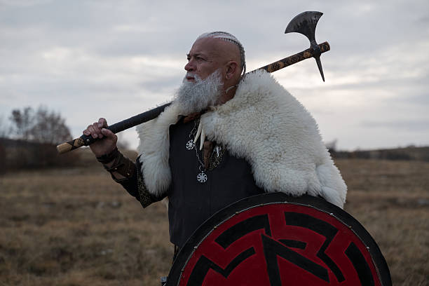Viking warrior with axe standing on mountain cliff, wearing fur cloak and leather armor, overlooking dramatic landscape. Historical Nordic fighter, strength and adventure concept.