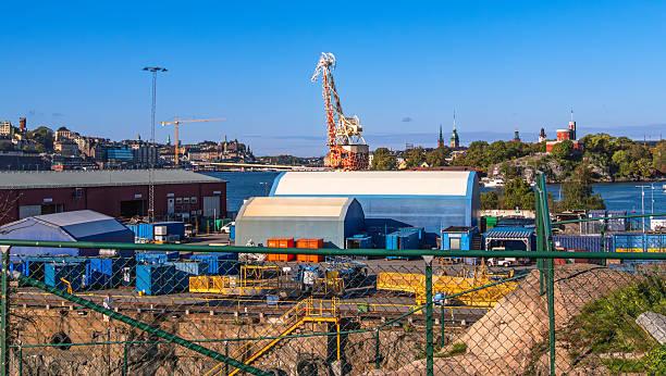 Industrial shipyard with cranes, containers, and buildings near water.