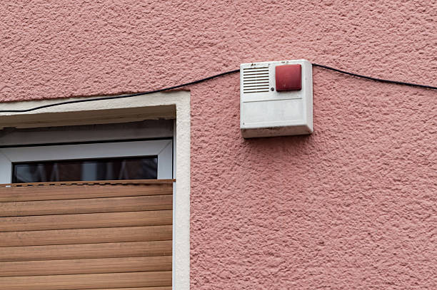Security alarm box mounted on a residential building's pink exterior wall