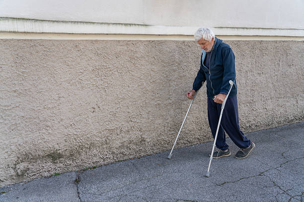 Senior man walking on the street, along the pavement using crutches after hip operation.
