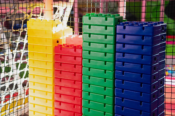 Tall stacks of vibrant plastic building blocks in yellow, red, green, and blue displayed inside an indoor children play zone with safety netting and colorful structures