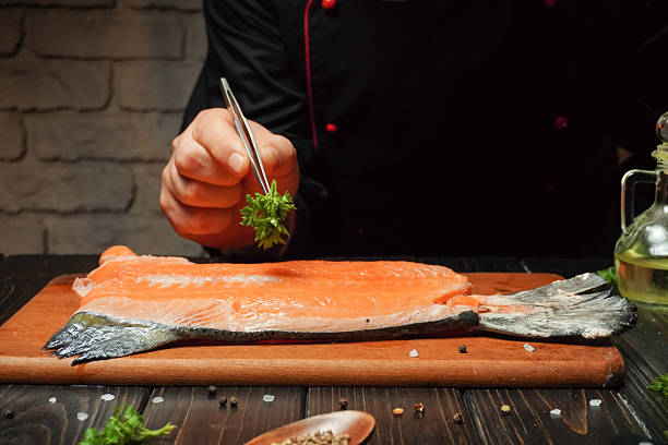 A chef carefully arranges herbs on a raw salmon fillet while working in a warm, inviting kitchen. Soft lighting creates a relaxing ambiance in the space