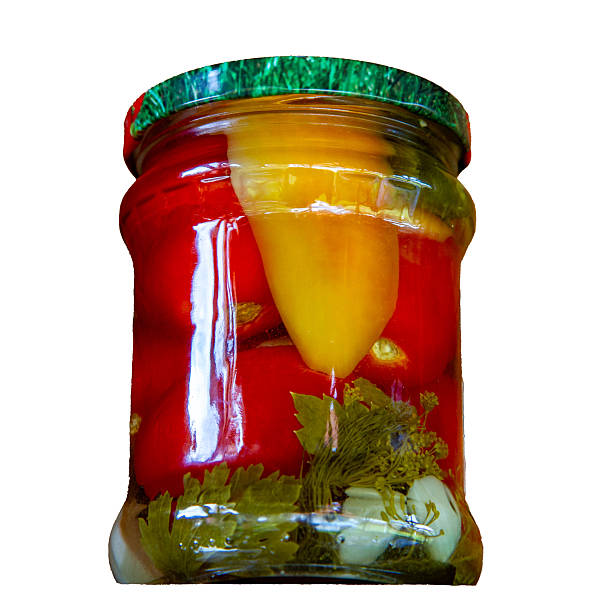 A glass jar filled with homemade pickled vegetables—tomatoes, peppers, herbs, and garlic—preserved in brine and isolated on a white background. Rustic organic food, traditional canning.