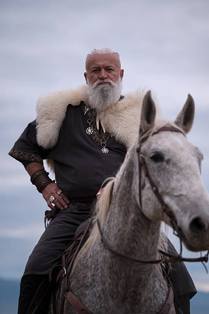 istock A majestic Viking chieftain on a dappled grey horse, clad in a fur cloak, surveys a desolate, mountainous landscape under a dramatic cloudy sky, exuding power and presence. 2246945577
