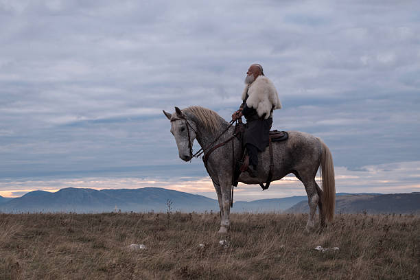 istock A majestic Viking chieftain on a dappled grey horse, clad in a fur cloak, surveys a desolate, mountainous landscape under a dramatic cloudy sky, exuding power and presence. 2246945700