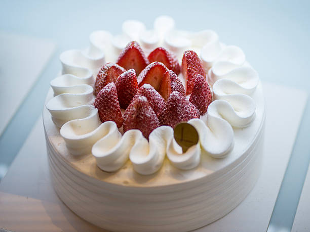 Close-up of a round strawberry and cream cake topped with fresh halved strawberries and whipped cream swirls, captured in bright, soft light for a fresh, elegant look.
