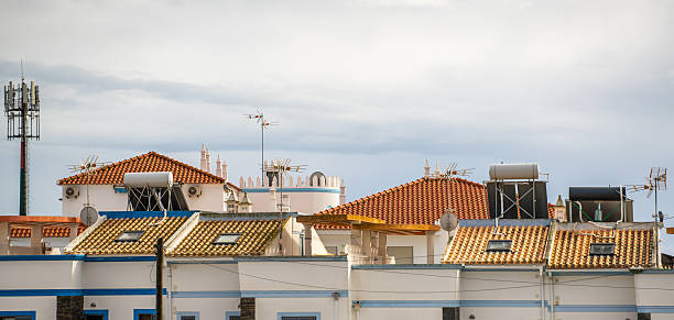 Traditional tiled rooftops equipped with solar water heaters, satellite dishes, and antennas under a cloudy sky