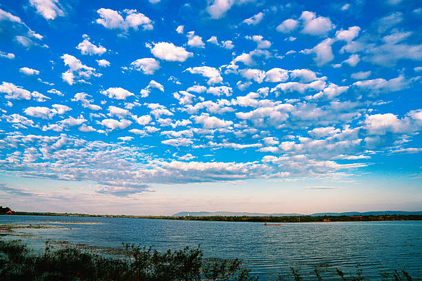 The sky is blue with many clouds. The water is calm and the sky is clear. The clouds are scattered throughout the sky