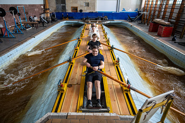 Top view of exhausted athletes rapidly rowing on simulator, working on synchronized techniques. Rowers hone coordination, endurance and breathing efficiency, male crew in aquatic water sports
