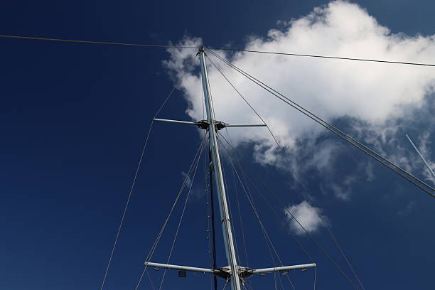 Tall sturdy mast of a sailboat stands out vividly against the bright blue sky