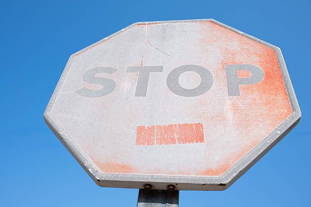 Weathered octagonal stop sign having its red color bleached by sun exposure, appearing old and scratched against a bright blue sky, symbolizing limitations and end of road