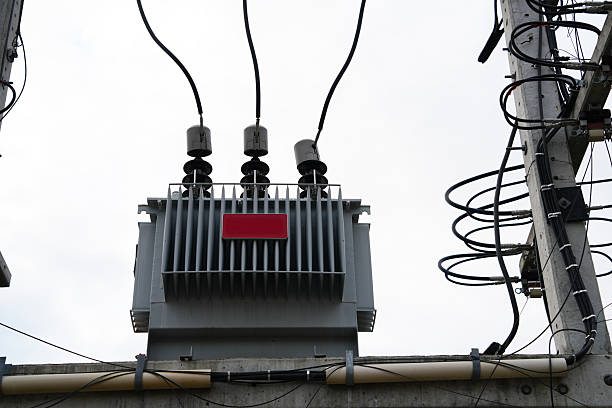 A large power station with three tall towers and a red box on top. The red box is labeled high voltage.