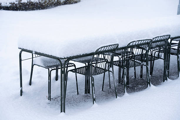 Metal chairs and a table sit outside, heavily laden with a thick layer of freshly fallen snow.