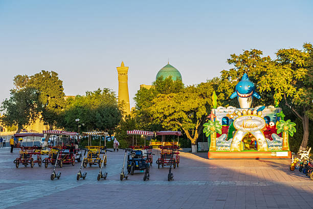 Bukhara, Uzbekistan - August 2, 2025. Display of a broad collection of steps, and carts for tranporting tourist, along with an inflatable play castle line the streets of Bukhara, with the famous mosque in the background.