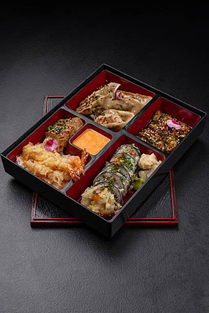 Japanese style bento box with sushi, kimchi, tofu, tempura and sauce on dark background isolated