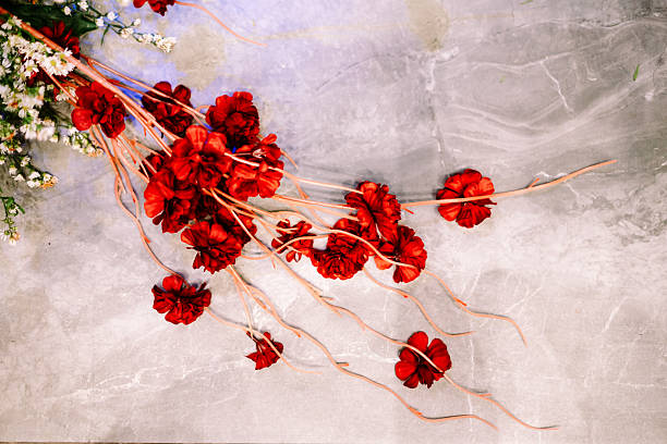 A beautiful arrangement of vibrant red artificial flowers and delicate white filler blossoms displayed elegantly on a textured gray stone surface. Perfect for festive, romantic, or decorative